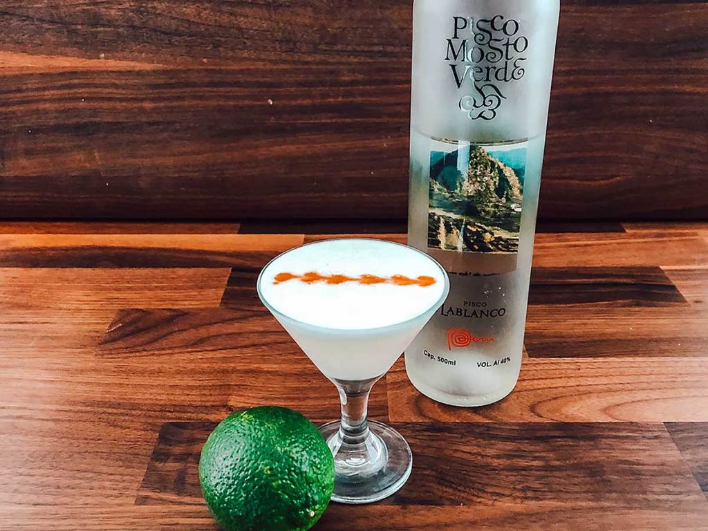 Pisco Sour cocktail with lime and Pisco bottle