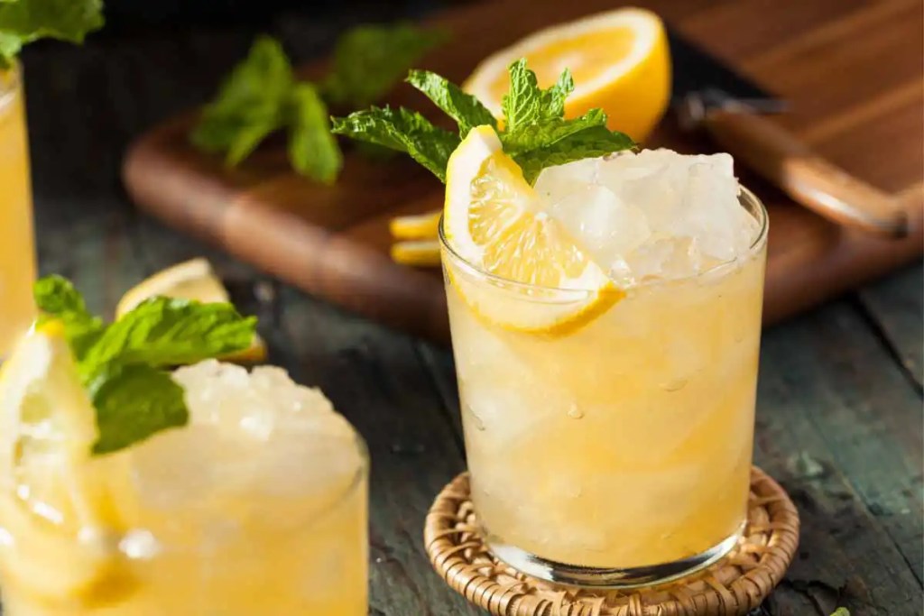 Refreshing bourbon smash cocktail garnished with a lemon wedge and fresh mint, perfect to serve as a Thanksgiving signature cocktail at your next holiday get together. Served over crushed ice in a glass, this citrusy and minty drink adds a zesty and vibrant flavor to a Friendsgiving celebration.