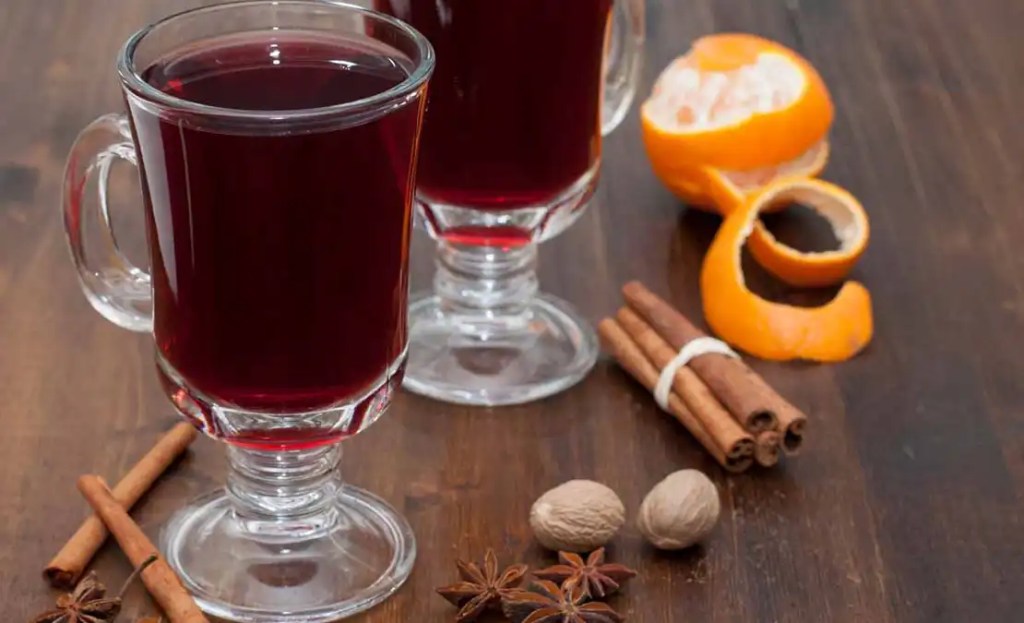 Two glasses of spiced mulled wine with ingredients like cinnamon sticks, star anise, nutmeg, and orange peel, a warming Friendsgiving drink idea. Served hot in glass mugs, this cozy and aromatic drink adds a comforting touch to any Friendsgiving celebration.