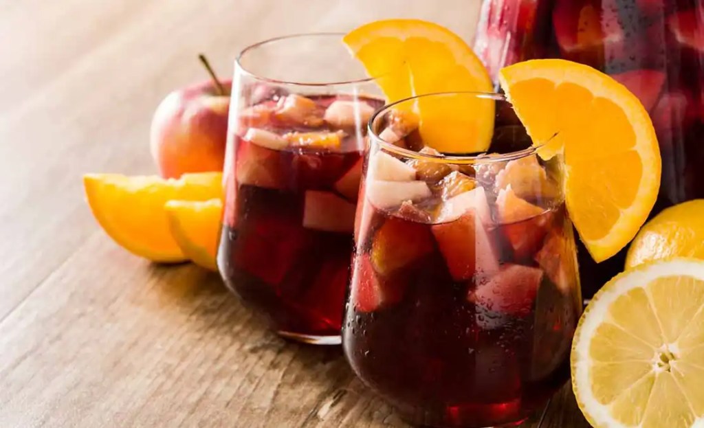 Two glasses of fruity red sangria, garnished with orange slices, perfect for Friendsgiving drink ideas. The sangria is filled with fresh fruit pieces like apples and oranges, adding a vibrant and refreshing touch to any Friendsgiving celebration.