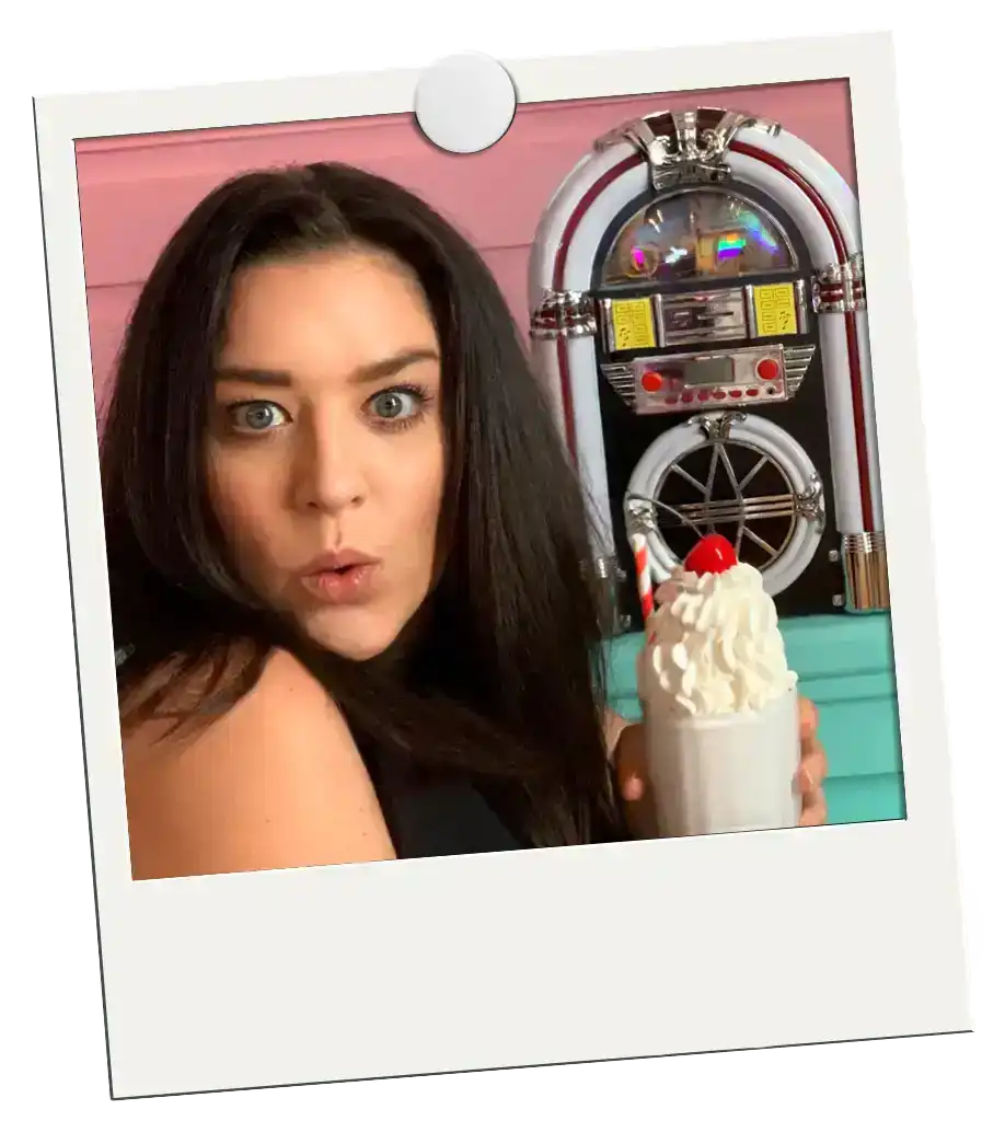 Freebies Polaroid of Jordan holding a cup topped with whipped cream and a cherry in front of a juke box